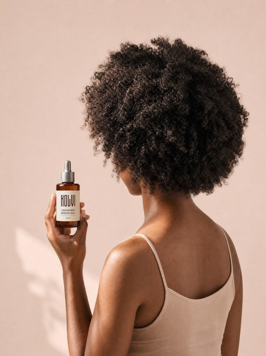 CROWNED Serum No.1 held beside natural coiled hair in warm morning light